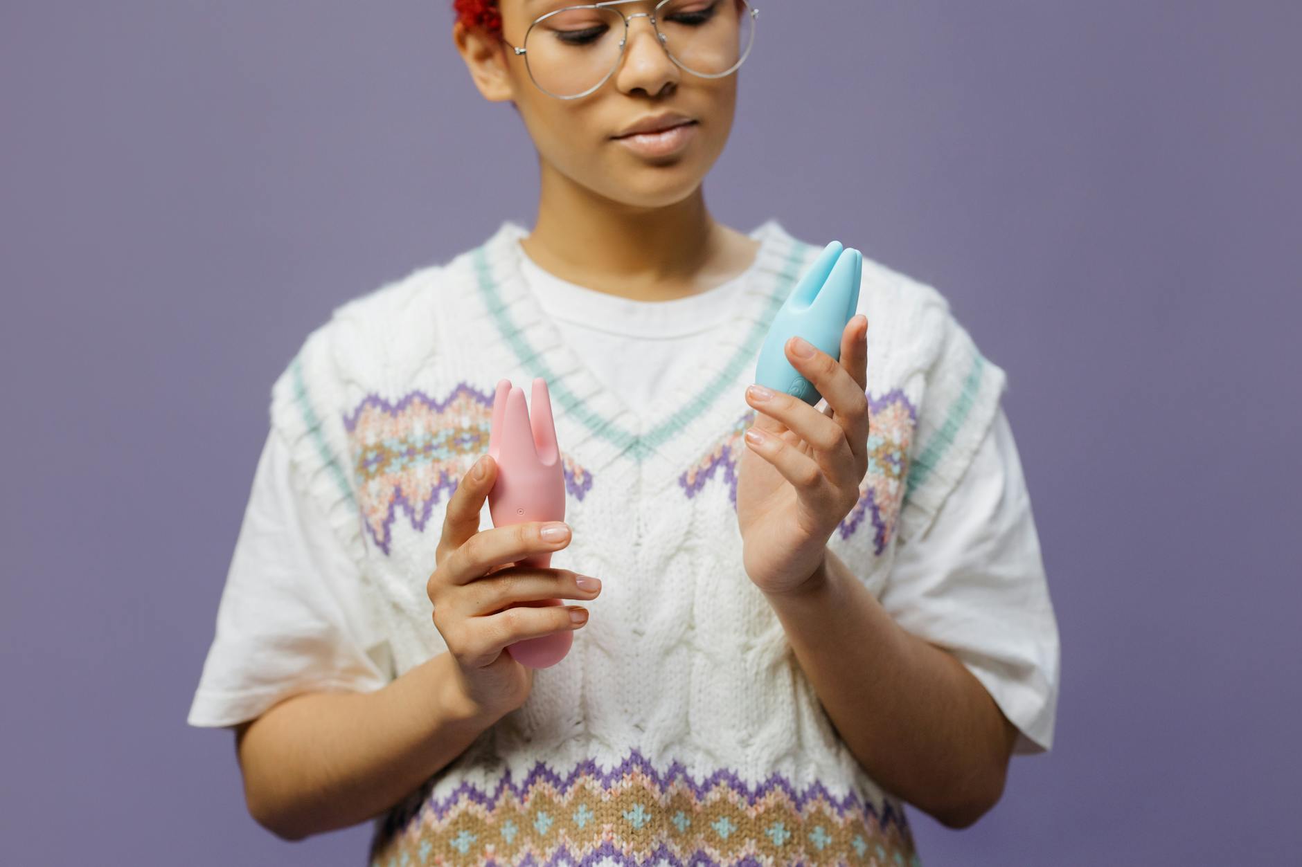 Vrouw met bril die blauwe en roze siliconen vibrators voorzichtig vasthoudt