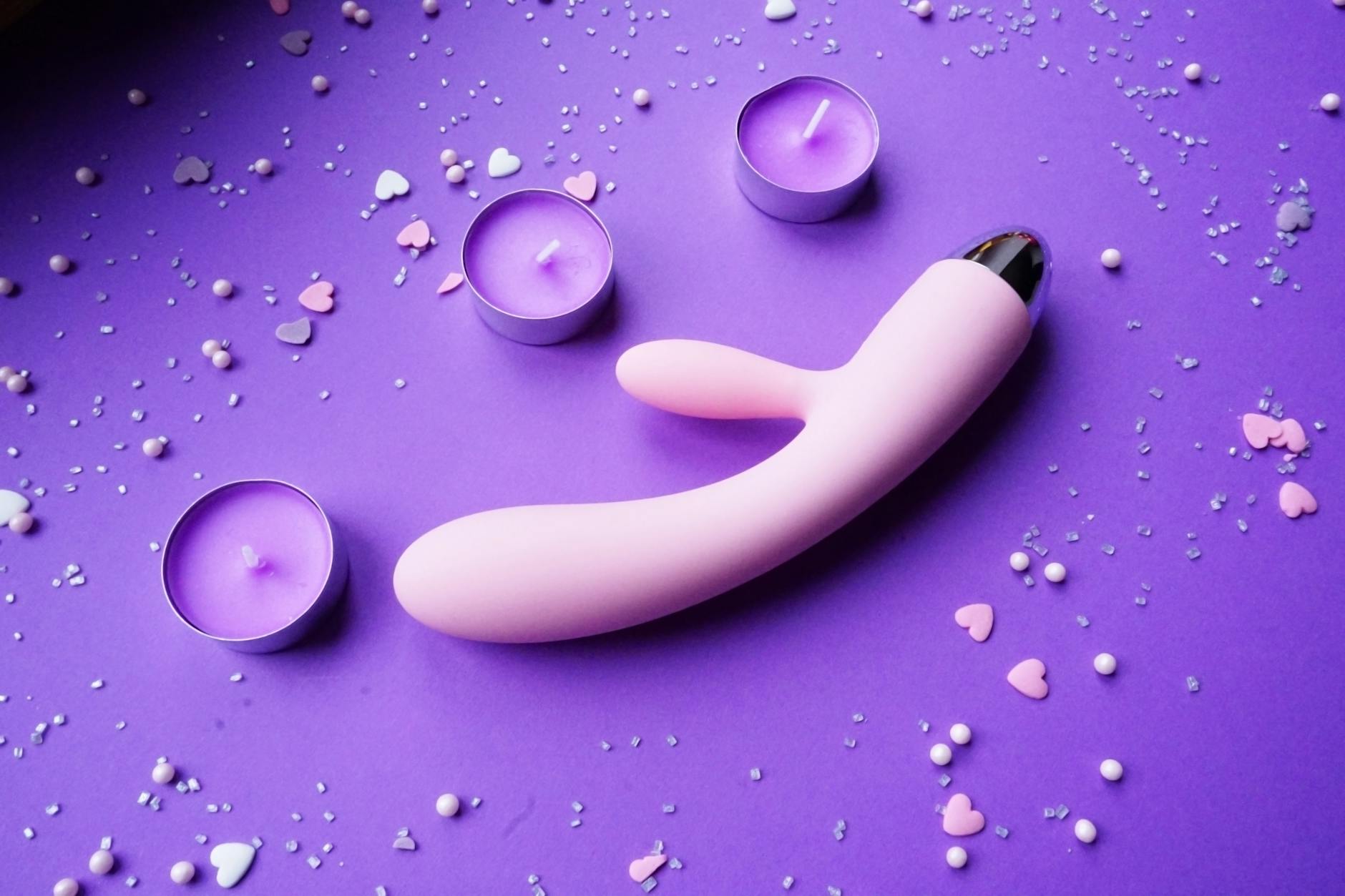 Roze citroenvibrator op paarse ondergrond met hartvormige confetti en kaarsen voor een romantische sfeer